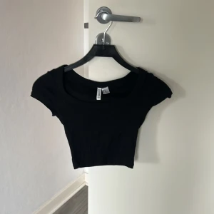 Svart croppad topp  - Svart croppad topp från HM med korta ärmar och rundad halsringning. Enkel och stilren design som passar perfekt till jeans eller kjol. Mjuk och stretchig bomullskvalitet för en bekväm känsla.