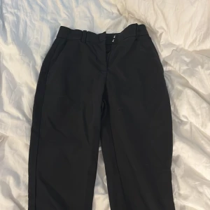Svarta kostymbyxor från H&M, stl 34 - Snygga svarta kostymbyxor från H&M i storlek 34. De har en klassisk rak passform med midja och bälteshällor, perfekta till en clean och stilren look. Materialet är mjukt och känns bekvämt mot huden, passar dig som gillar minimalistisk stil.