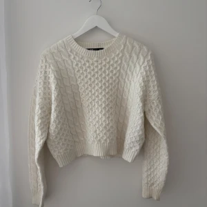 Vit stickad tröja med kabelmönster - Säljer en supermysig vit stickad tröja med klassiskt kabelstickat mönster. Tröjan har rund halsringning, ribbade muddar och lång ärm. Perfekt att slänga på sig när det är kyligt ute.