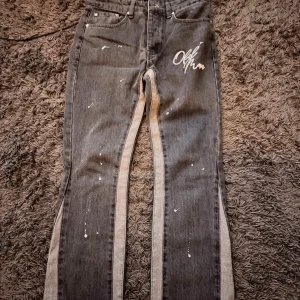 Grå flared jeans - Unika flared grå jeans med vita sidor och coola färgstänk framtill. Byxorna har rak passform och klassisk femficksdesign. Snyggt broderad text på ena fickan ger extra edge. Perfekta för dig som vill sticka ut med din stil.