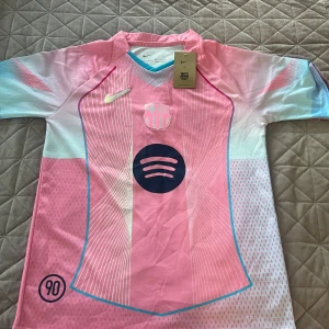 Barça Lamine Yamal rosa matchtröja - Snygg FC Barcelona fotbollströja från Nike i rosa och ljusblå toner med vita detaljer. Kortärmad med tryckta linjer, klubbmärke, Spotify-logga och nummer 10 med Lamine Yamal på ryggen. Tillverkad i lätt, ventilerande material som passar perfekt på planen.