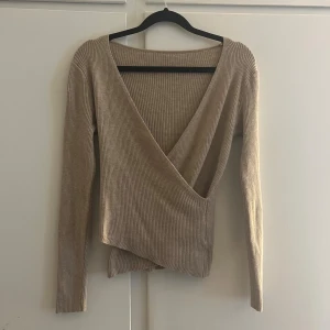 Beige omlottopp - Snygg beige omlottopp med ribbad struktur. Långärmad modell som sitter väldigt skönt. Har för mig att storleken är M men skulle säga att det passar en S oxå (lappen är inte kvar). 