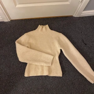 Beige ribbad polotröja från H&M - Supermysig beige polotröja från H&M i ribbstickat material. Tröjan har hög krage och långa ärmar, perfekt för kyliga dagar. Enkel och stilren modell som är lätt att matcha med allt. Sitter snyggt och är riktigt skön att ha på sig.