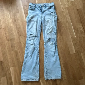 Ljusblå bootcut jeans med slitningar - Jättesnygga bootcut jeans med hål och slitningar! De är i storlek 32 men ganska uttöjda så skulle säga att de passar mer som 34. De är i använt skick och har två ganska stora hål vid de inre sidorna på bakfickorna (bild 3) men borde lätt kunna lagas. 