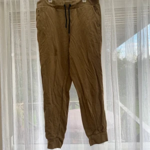 Beiga mjukisbyxor med snörning - Säljer ett par beiga mjukisbyxor med svarta snören i midjan och muddar vid bensluten. Byxorna har en avslappnad passform och är tillverkade i mjukt bomullsmaterial. Perfekta för chill dagar eller när du vill vara extra bekväm.