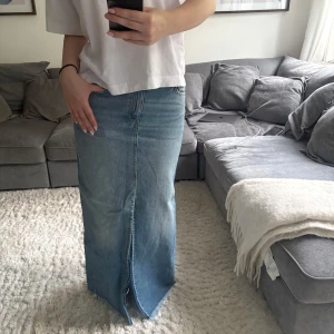 Lång jeanskjol med slits - Säljer en snygg lång jeanskjol i ljusblå denim med rak passform och en slits framtill. Näst intill oanvänd då den är lite i minsta laget. Önskas fler bilder eller mer info skriv privat!🥰