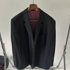 Svart kostym från Alexandre London Savile Row - Klassisk svart skräddarsydd kostym från Alexandre London Savile Row. Kostymen består av en kavaj med tre knappar och matchande byxor. Kavajen har en elegant design med en ficka på bröstet och två fickor på sidorna. Fodret är i en kontrasterande färg som ger en sofistikerad touch.. Köpt i London där den också tillverkades och har sen dess har den väl omhändertagits. Kostymen har en historia av affärer och företagande internationellt. Vid exakta passmått ta gärna kontakt. Nypris: 3000 - 3500 euro