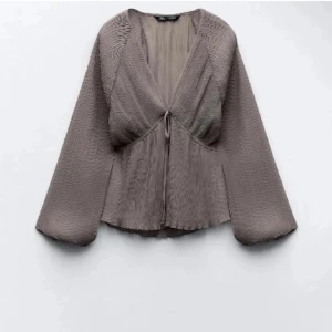 Beige blus med knyt och vida ärmar - Jättefin grå/beige blus. Blusen har vida, långa ärmar och tunt tyg. Säljer då den inte kommer till användning längre💗