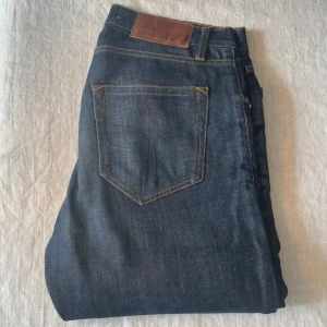 Mörkblå jeans från tiger of Sweden  - Snygga mörkblå jeans från T/J i modellen Pistolero, storlek 28/32. Klassisk femficksdesign med kontrastsömmar och läderpatch bak i midjan. Jeansen har en rak passform och är tillverkade i slitstarkt denimtyg.