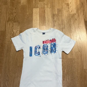 Vit Dsquared2 ICON t-shirt - Vit t-shirt från Dsquared2 med stort tryck 'ICON' i blått och rött framtill. Snygg grafisk design med färgglada detaljer och Dsquared2-logga. Klassisk rund hals och korta ärmar. Tillverkad i mjuk bomull som är skön att ha på sig. Köpt för 850 använd ganska mycket
