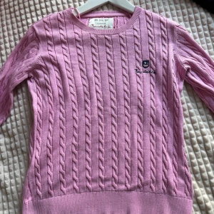 Rosa kabelstickad tröja från Bondelid - Supersöt rosa kabelstickad tröja från Bondelid med broderad logga på bröstet. Tröjan har rund halsringning, långa ärmar och ribbade muddar. Priset går att diskutera.