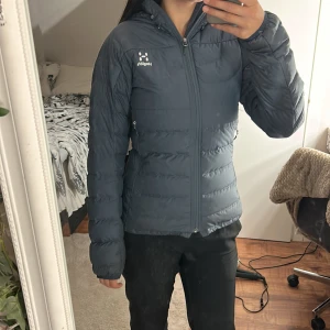 Mörkblå dunjacka från Haglöfs. Två stora fickor där fram en stor ficka innanför jackan. Väldigt skön och varm  - Säljer en mörkblå dunjacka från Haglöfs med huva och dragkedja framtill. Jackan har två praktiska fickor med dragkedja och quiltad design som håller värmen. Perfekt för kyliga dagar och snygg till både jeans och träningsbyxor.