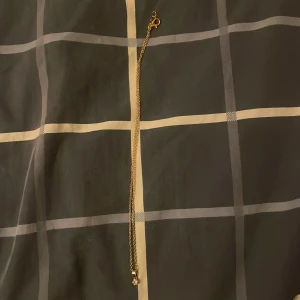 Guldigt halsband med liten sten - Snyggt halsband i guldton med tunn kedja och en liten, klar sten som hänger i ett enkelt fäste. Perfekt för dig som gillar stilrena och klassiska smycken med en touch av elegans. Kedjan är smal och ger ett diskret men lyxigt intryck.