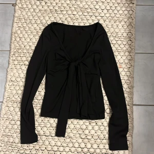 Svart långärmad topp med knyt - Säljer en svart långärmad topp med snygg knytning framtill i storlek S/xs. Säljer för att den är för liten, inte använd mer än 3 gånger. 