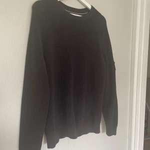 Svart stickad tröja Calvin Klein Jeans - Svart stickad tröja från Calvin Klein Jeans med grovstickad struktur och rund halsringning. Tröjan har en stor CK-logga på ärmen och långa ärmar. Perfekt för dig som gillar en clean och stilren look.