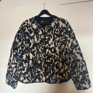 Leopardmönstrad quiltad jacka från Zara - Säljer en quiltad jacka från Zara med mönster i svart och beige, tryckknappar framtill och två fickor. materialet är mjukt och bekvämt. Mycket använd men inget som syns!