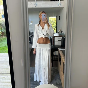 Vit långkjol med volanger - Superskön vit långkjol med bred midjeresår och flera volanglager. Kjolen har en flowy och luftig känsla, perfekt för varma dagar. Stilren och enkel att matcha med crop tops eller skjortor. Materialet känns mjukt och lätt mot huden.