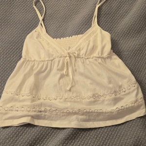 Vit linnetopp från Stradivarius - Supersöt vit linnetopp från Stradivarius med tunna axelband, v-ringning och knyt framtill. Toppen har spetsdetaljer och smockad rygg. Toppen är inte använd och har en skön passform! Passar perfekt till jeans med en kofta eller shorts till sommaren! Ny pris 250! Slutsåld i butik! Köpt i Spanien! Skriv om du är intresserad eller har några frågor!!🫶🩵🍁☀️