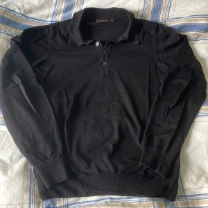 Blå pikétröja från Oscar Jacobson - Blå pikétröja från Oscar Jacobson, tillverkad i Italien. Tröjan har lång ärm, krage och tre knappar framtill. Perfekt för dig som gillar en stilren outfit eller en mer uppklädd look