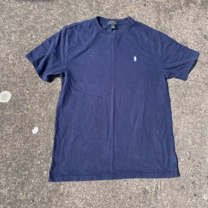Ralph lauren t shirt  - Snygg mörkblå t-shirt från Polo Ralph Lauren med klassisk vit logobrodering på bröstet. Modellen är normal passform med rund hals och korta ärmar. Tillverkad i mjuk bomull som är skön mot huden. Perfekt för dig ”som vill skaffa nya Grisch kläder” och enkel att matcha med jeans eller shorts, tröjan e väldigt fräsch och clean och killen på bilden är cirka 185, storlek S/m passar båda, skicket är som nytt, hör av dig vid minsta lilla fråga🙌🏼