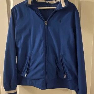 Blå vindjacka från Polo Ralph Lauren - Snygg blå vindjacka från Polo Ralph Lauren i storlek S i fint skick men några få defekter på en av ärmarna och på något annat ställe som man knappast märker! 