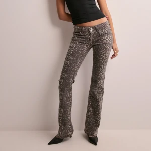 Leopardmönstrade bootcut jeans - Snygga bootcut jeans med leopardmönster i bruna och beige toner. Byxorna har låg midja, klassisk femficksdesign och stängs med dubbla knappar. Perfekta för dig som vill sticka ut med en trendig och djärv look.