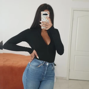 Svart v-ringad långärmad topp - Snygg svart långärmad body med djup v-ringning och slim passform. Perfekt att matcha med jeans eller kjol för en clean och stilren look. Materialet känns mjukt och stretchigt mot kroppen, vilket gör den bekväm att bära hela dagen.