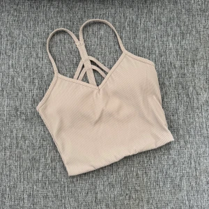 Beige ribbad linnetopp från Aim'n XS - Supersnygg beige ribbad linnetopp från Aim'n med tunna axelband och coola korsade detaljer i ryggen. Perfekt för träning eller chill dagar. Mjuk och stretchig känsla tack vare materialmixen av nylon och spandex.