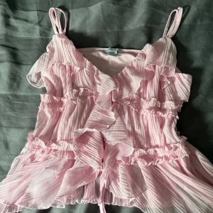 Rosa volangklänning från new yorker  - Supersöt rosa kortklänning från new yorker med tunna axelband och volanger över hela blusen. Materialet är lätt och luftigt med ett randigt mönster och transparenta detaljer. Perfekt för sommarens alla tillfällen när du vill känna dig extra gullig. I storlek L men passar till xs och S oxå💕 andvänt 1 gång 