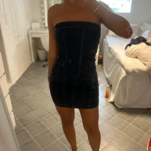 Mörkblå tubklänning i jeans - Säljer en mörkblå, tight tubklänning i jeansmaterial med markerade sömmar. Klänningen är kort och axelbandslös, perfekt för dig som gillar en enkel men snygg look. Passformen är slim och materialet är stadigt denim.