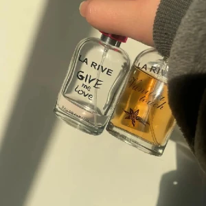 La Rive parfymduo Give Me Love & Vanilla Touch - Två stilrena parfymflaskor från La Rive: Give Me Love med transparent vätska och rosa detalj på korken, samt Vanilla Touch med varm bärnstensfärgad vätska och vaniljblomma på flaskan. Båda i glasflaskor med rundad form och svart text.