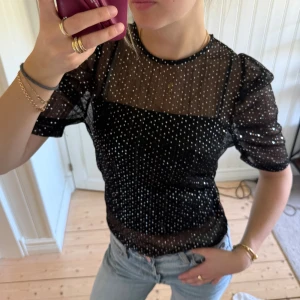 Svart glittrig topp från Gina Tricot - Säljer en svart transparent topp från Gina Tricot i storlek XS. Toppen har glittriga prickar över hela tyget, korta puffärmar och rund halsringning. Har ett linne under så den är egentligen helt transparent