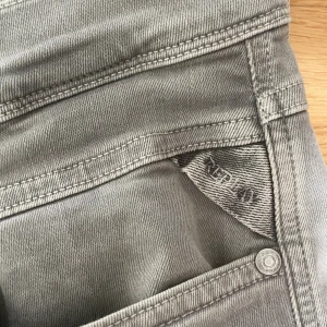 Gråa Replay jeans flex - Snygga grå jeans från Replay med klassisk femficksdesign och raka ben. Jeansen har en stilren look med diskreta detaljer och Replay-logga på fickan. Perfekta för dig som gillar en clean och modern stil. Materialet är mjukt och stretchigt för extra komfort.