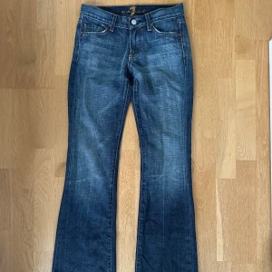Low waist bootcut jeans - Super snygga blå lågmidjade bootcut jeans från 7 For All Mankind med klassisk femficksdesign. Baksidan har coola detaljer med nittar på fickorna. Jeansen är 100% bomull. De är i en mörk tvätt med små slitningar i modellen för en vintage/2000s vibe. Jeansen är i superfint skick, nästintill använda. Köpte på Vinted men de var tyvärr för små🥲. Storlek: 24. Platta mått: innerbenslängd:76cm, midja:33cm, höft:39cm, gren:19cm och lår:20cm. Nypris: 1200kr. Säljer för: 350kr!
