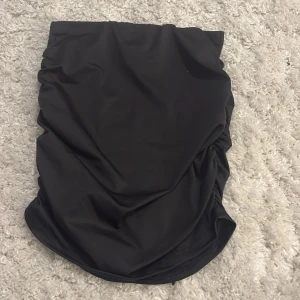 Svart kortkjol med rynk från SHEIN - Svart kortkjol från SHEIN i storlek XS. Kjolen har en tight passform och snygga rynkade detaljer längs ena sidan som ger en cool och trendig look. Tillverkad i ett stretchigt syntetmaterial som sitter skönt på kroppen.