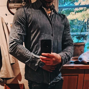 Filippa K-skjorta  - Mörkblå/jeansfärgad bomullsskjorta med klassisk krage och knäppning framtill från Filippa Kl. Skjortan har lång ärm och en något slim passform som framhäver axlar och armar. Perfekt för dig som gillar stilrena och enkla plagg med en modern touch. Har blivit lagad i armhålan samt normalt bruksslitage. Inget som syns ens om du lyfter armarna. 