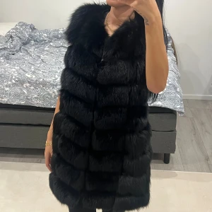 Svart lång pälsväst i äkta päls - Säljer en svart, fluffig och lång pälsväst. Västen är tillverkad av 100% äkta päls och har ett lyxigt, glansigt foder i silke och polyester. Storlek S-M