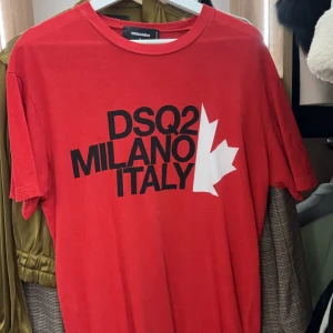  DSQUARED2 t-shirt - Snygg röd t-shirt från DSQUARED2 med svart tryck 'DSQ2 MILANO ITALY' och en vit lönnlövsgrafik på framsidan. Klassisk rund hals och korta ärmar. Tillverkad i mjuk bomull, perfekt för dig som gillar streetwear med statement. Äkta!