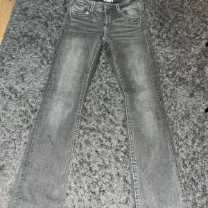 Grå bootcut jeans från Gina Tricot - Snygga lågmidjade grå jeans från Gina Tricot i bootcut-modell med markerade sömmar och klassiska fem fickor. Jeansen har knappar på bakfickorna och dragkedja fram. Perfekt för dig som gillar en lite retro vibe och vill ha ett par jeans med cool tvätt. Passar storlek s-m använda 2 gånger