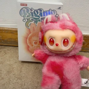 Pop Mart Bigimo Enami Love Edition - Pop Mart Bigimo Enami Love Edition samlarfigur i rosa plysch med unikt ansikte och öron. Levereras med originalförpackning. Figuren är i mycket gott skick, inga synliga defekter eller slitage. Perfekt för samlare eller som dekorativ prydnad.