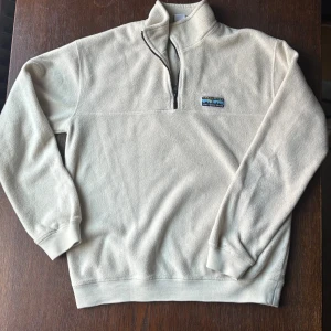Vit fleece half zip från JUNKYARD - Säljer en vit fleece-tröja från Junkyard med half zip och broderad logga på bröstet. Perfekt för hösten! Enkel och clean design som funkar till jeans eller mjukis. Mindre märke på vänstra arm (se bild), men märks inte.