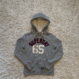 Grå hoodie från superdry med fodrad luva - Riktigt snygg grå hoodie från superdry med en fodrad luva vilket gör den extra varm. Topp skick utan defekter. Står storlek M men skulle säga att den som en S herr, tror att det är en dammodell igentligen o därför den sitter mindre. Tveka inte på o skriva vid fler frågor!