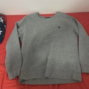 Grå sweatshirt från Polo Ralph Lauren - En stilren grå sweatshirt från Polo Ralph Lauren i storlek 14-16 år. Tröjan har rund hals, långärmade ärmar och ett diskret broderat Polo-logo på bröstet. Mjuk och skön, perfekt för chill dagar. Materialet är bomull och polyester. Jag säljer den här för att den är för liten för mig nu.