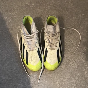 Adidas Crazyfast fotbollsskor gul/vit storlek 44 2/3 - Säljer ett par Adidas Crazyfast fotbollsskor i vitt och neongult med svarta ränder. Skorna har snörning, platt sula med dobbar och en sportig, smal siluett. Perfekta för dig som vill sticka ut på planen och få grymt grepp. Materialet är syntet och textil.