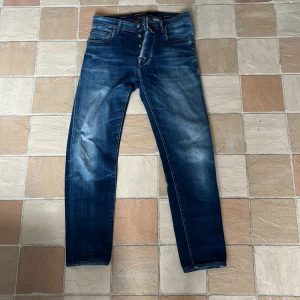 Blå jeans från Jacob Cohen storlek 29 - Snygga blå jeans från Jacob Cohen med coolt sliten tvätt och röda kontrastsömmar. Klassisk femficksmodell med knappgylf och unikt mönstrat innerfoder. Bak finns en röd patch med logga. Perfekt för dig som gillar detaljer och italiensk design.