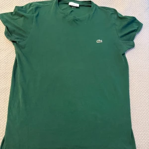 Grön t-shirt från Lacoste - Snygg grön t-shirt från Lacoste i bomull. Klassisk modell med rund halsringning, korta ärmar och den ikoniska krokodilloggan broderad på bröstet. Regular fit som sitter skönt om du har S i storlek.