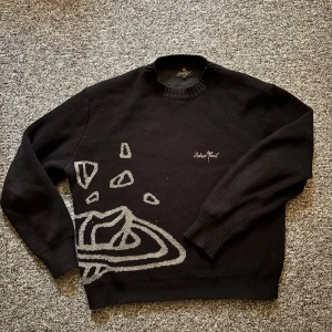 Svart stickad tröja Broken Planet L - Svart stickad tröja från Broken Planet i storlek L. Tröjan har grått rymdmotiv med planeter och stjärnor både fram och bak samt broderad logga på bröstet. Rund halsringning och ribbade muddar för en clean och modern look. Lite oversized för någon som är mellan 185-190cm.