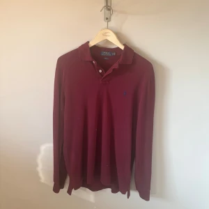 Långärmad pikétröja Polo Ralph Lauren - Säljer en vinröd långärmad pikétröja från Polo Ralph Lauren i slim fit. Tröjan har klassisk krage, knäppning vid halsen och den ikoniska broderade loggan på bröstet. Få tecken på användning, storlek L.