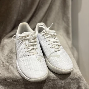 Vita Puma Adrenalite sneakers strl 38 - Säljer ett par fräscha vita Puma Adrenalite sneakers i storlek 38. Skorna har ett stilrent randigt mönster, klassisk snörning och rund tå. Ovandelen är i syntetmaterial och de har en platt sula som passar perfekt till en sportig look.