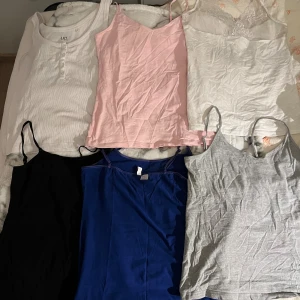 6-pack linne i olika färger - Säljer ett paket med sex linne-toppar i olika färger: vit, rosa, svart, blå, grå och en vit med spetsdetalj. 